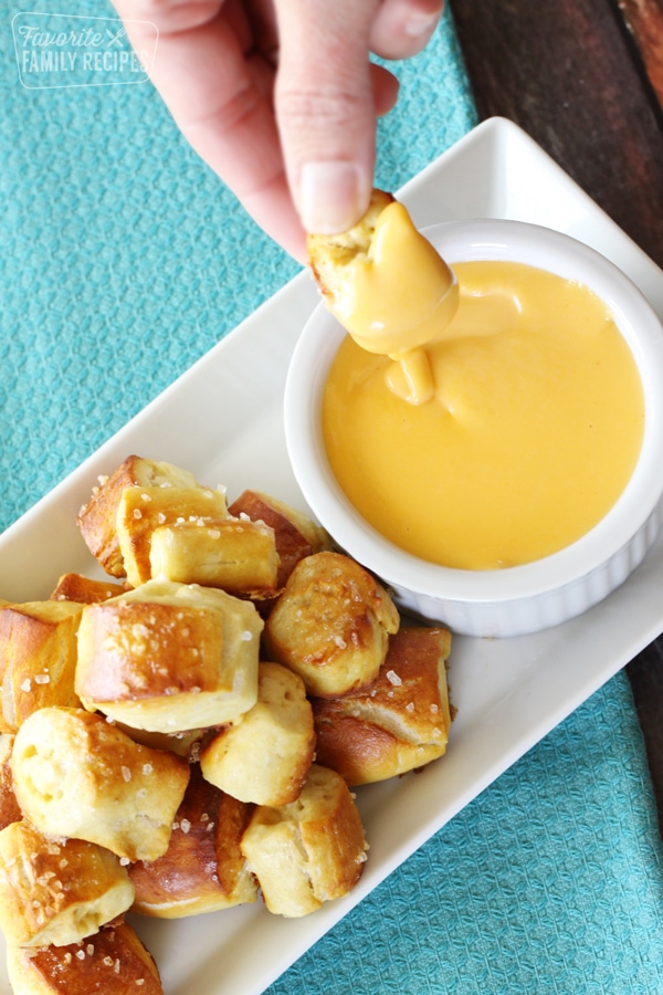 Golden pretzel bites being dipped in cheese.