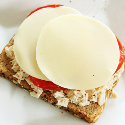 Slice of whole wheat bread layered with tuna fish, tomatoes, and provolone cheese