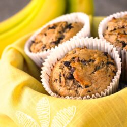 Banana chocolate chip muffins in a basket with yellow flower cloth.