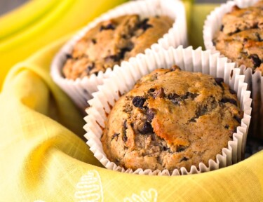 Banana chocolate chip muffins in a basket with yellow flower cloth.