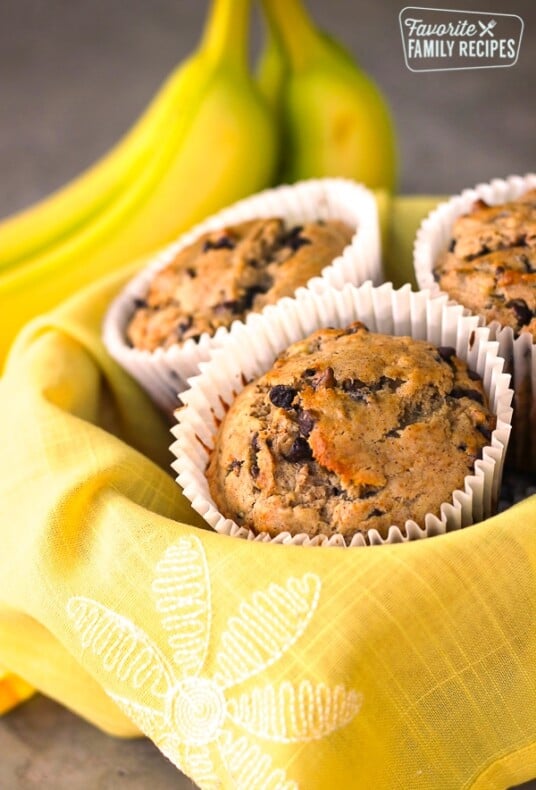 Banana chocolate chip muffins in a basket with yellow flower cloth.