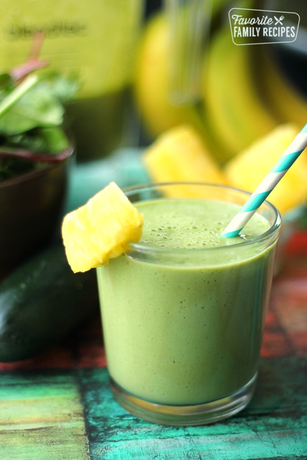 Cool Cucumber Green Smoothie with a slice of pineapple on the rim and a blue straw.