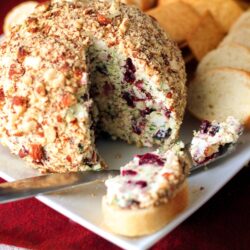 Cranberry Almond Bacon Cheese Ball with a slice taken out and pieces of bread on the side.