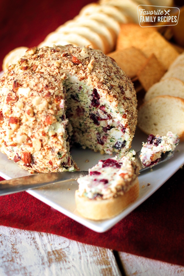 Cranberry Almond Bacon Cheese Ball with a slice taken out and pieces of bread on the side.
