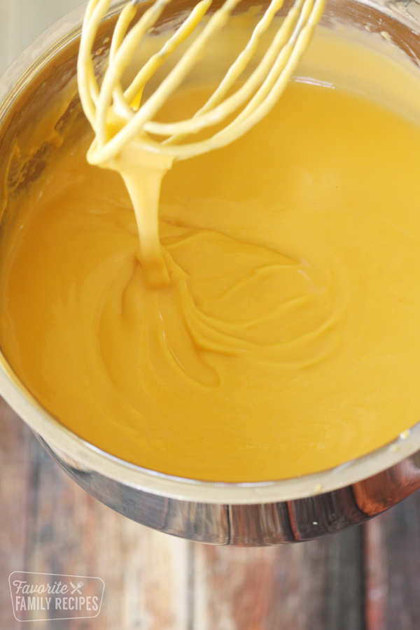Cheese sauce in a sauce pan with a whisk pulling away the cheese. 