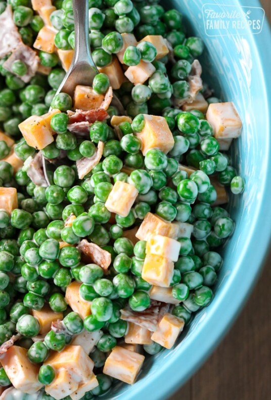 Creamy Green Pea Salad with bacon and cheese being scooped from a turquoise bowl with a serving spoon