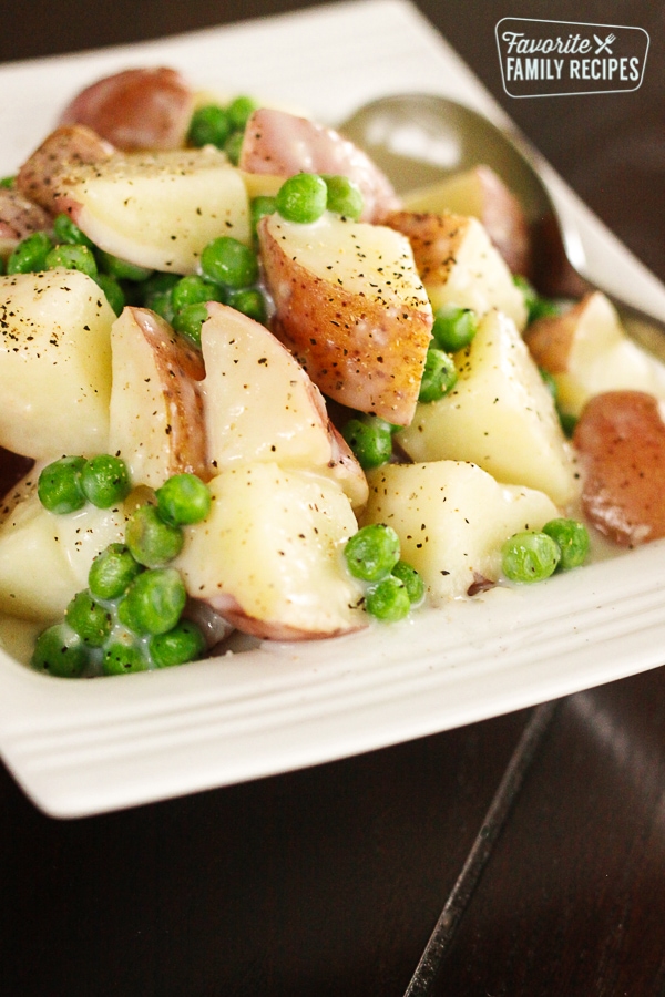 Creamy Potatoes and Peas on a white plate with a spoon on the side.