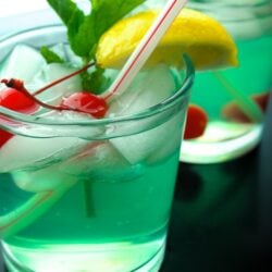 Two Mint Julep drinks served in clear glasses with a lemon slice, maraschino cherries, and a mint leaf for garnish