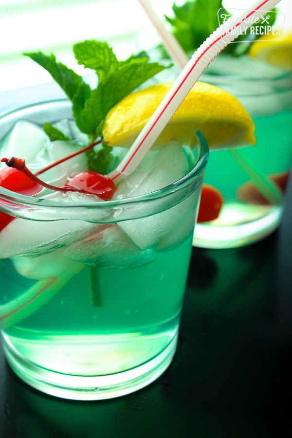 Two Mint Julep drinks served in clear glasses with a lemon slice, maraschino cherries, and a mint leaf for garnish