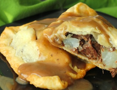 Two Irish Pasties filled with beef and potatoes on a black plate with a green napkin