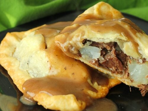 Two Irish Pasties filled with beef and potatoes on a black plate with a green napkin