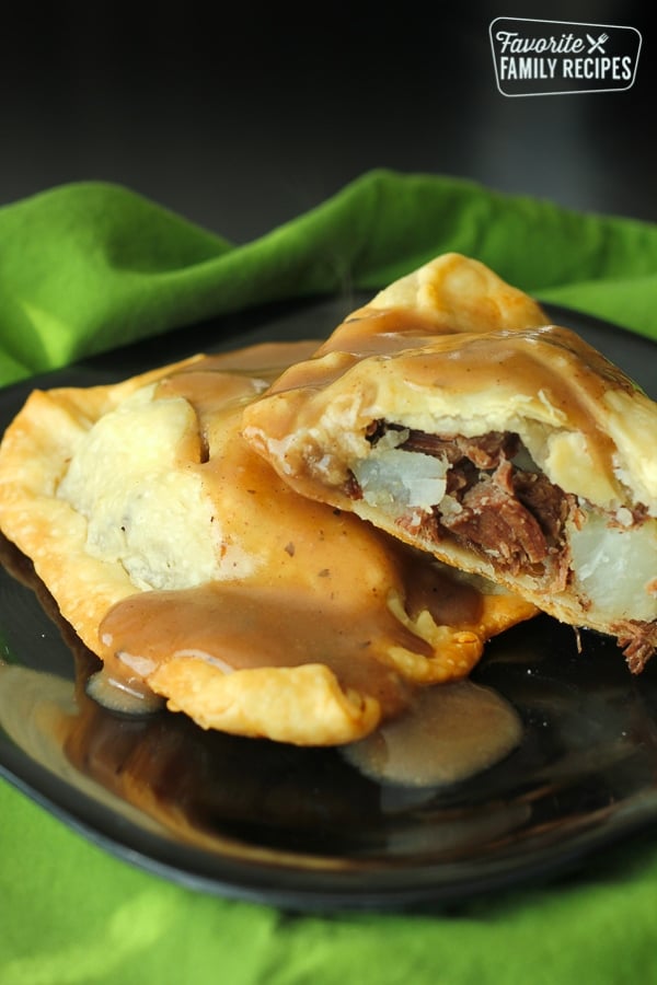 Two Irish Pasties filled with beef and potatoes on a black plate with a green napkin