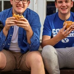Two teenagers sitting on the back porch eating chicken sandwiches