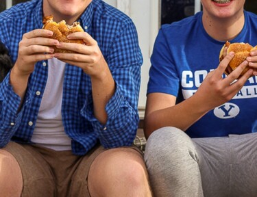 Two teenagers sitting on the back porch eating chicken sandwiches
