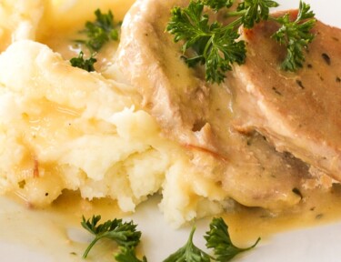 Easy Crock Pot Pork Chops with sauce and mashed potatoes on a white plate.