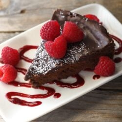 Slice of Easy Flourless Chocolate Cake topped with powdered sugar and raspberries.