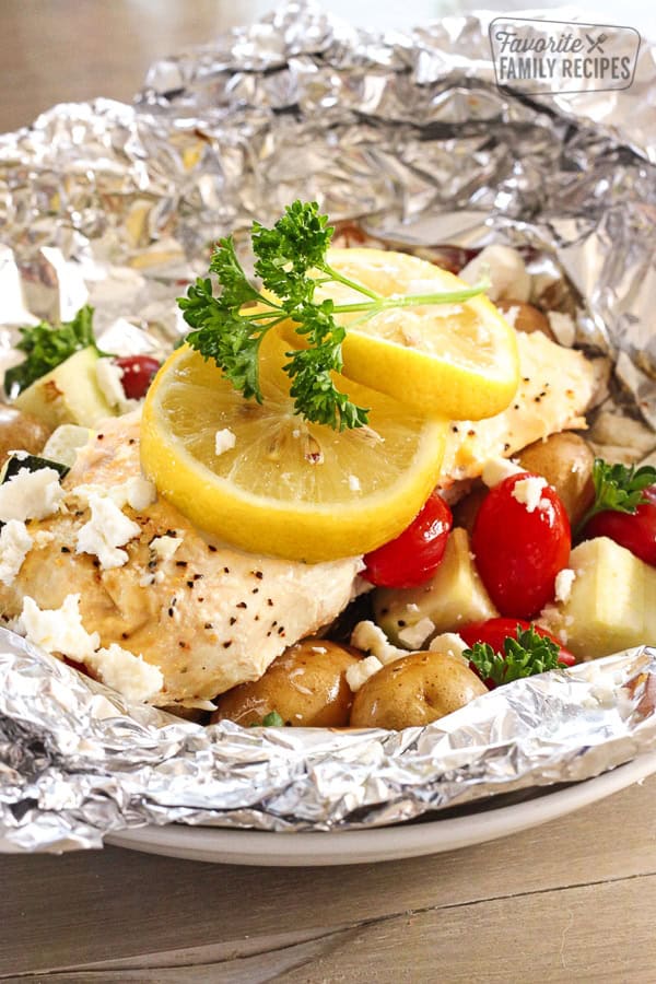 These Chicken Foil Packets with Vegetables are an easy summertime meal with virtually no clean up. Perfect for camping or just an easy dinner at home! Greek Lemon Chicken Foil Packets with Vegetables and lemon slices topped with a garnish.