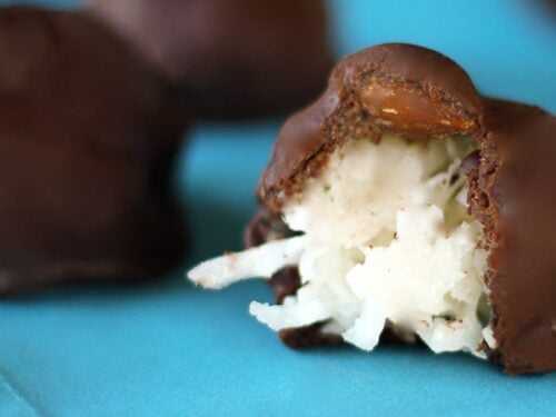 Homemade Almond Joys on a blue napkin with one almond joy cut in half showing coconut center