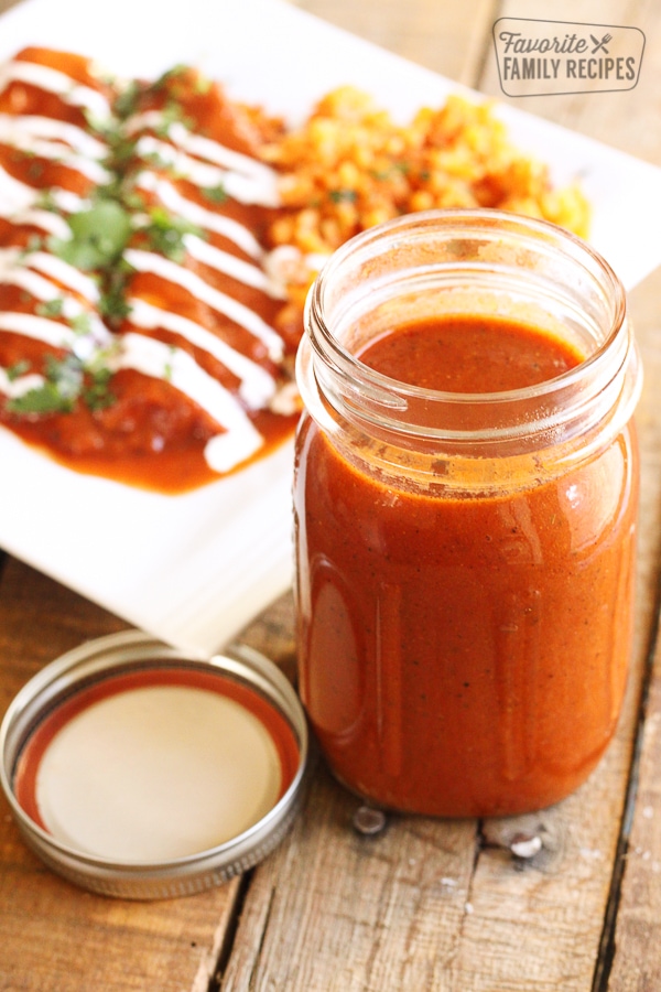 Homemade Enchilada Sauce in a mason jar with enchiladas in the background.