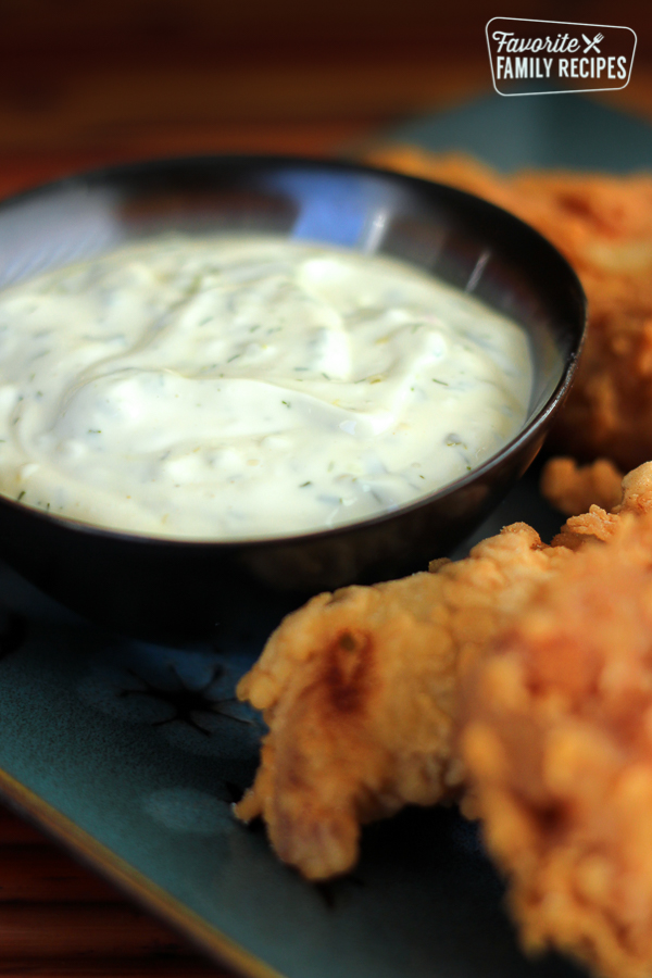 Homemade Tartar Sauce in a black bowl with fish on the side.