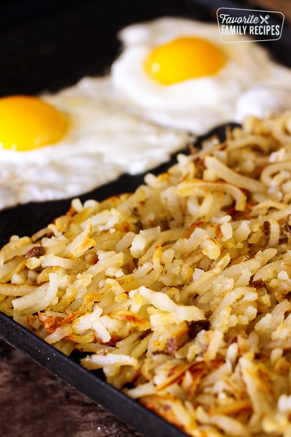 Homemade hash browns made from potatoes served on a cast iron skillet with two fried eggs on the side