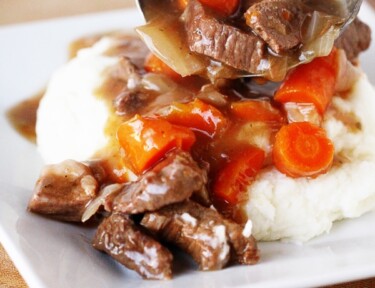 Instant Pot Beef Goulash poured over mashed potatoes on a white plate.