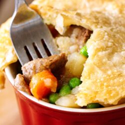 A red dish filled with Instant Pot Beef Pot Pie with chunks of beef, carrots, potatoes and peas