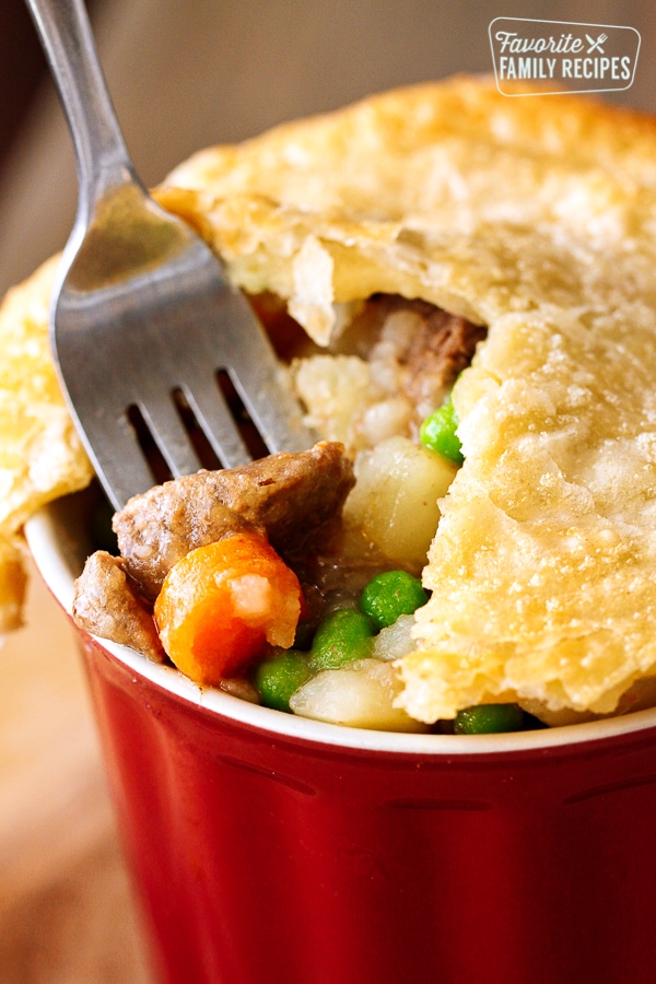 A red dish filled with Instant Pot Beef Pot Pie with chunks of beef, carrots, potatoes and peas.