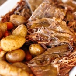 Instant Pot Sunday Beef Roast shredded on a serving plate with potatoes and carrots