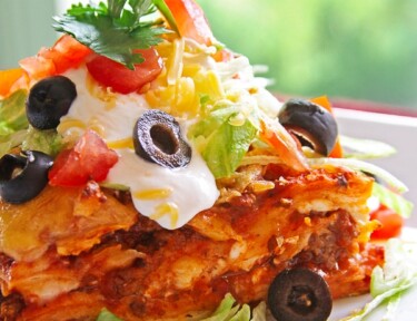 A slice of Mexican Lasagna topped with cheese, olives, lettuce, and cilantro on a white plate.