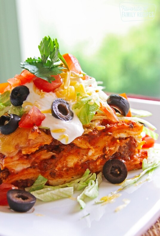 A slice of Mexican Lasagna topped with cheese, olives, lettuce, and cilantro on a white plate.
