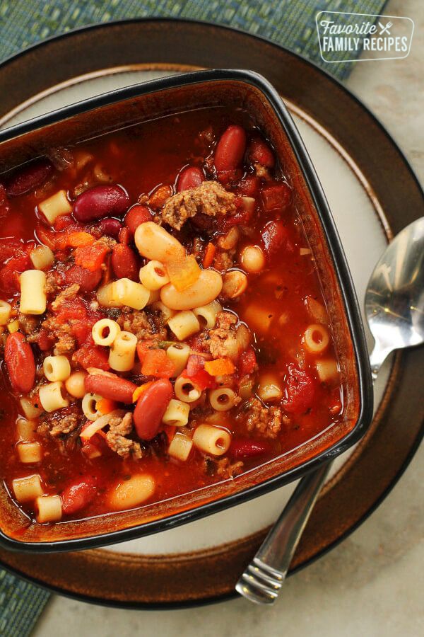 Our Version of Olive Garden’s Pasta E Fagioli Soup in a square bowl on a plate with a spoon on the side.