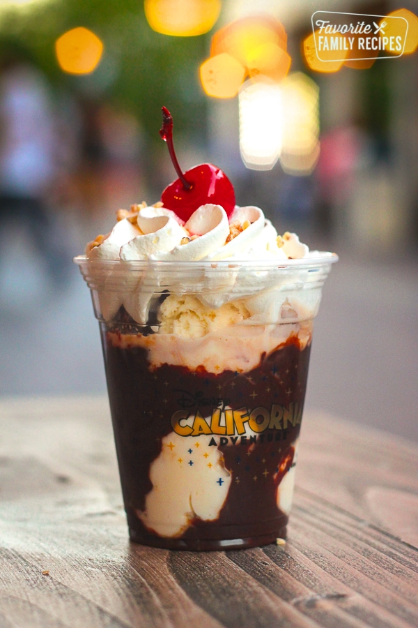 Ice cream with hot fudge in a plastic cup with whipped cream and a cherry on top.