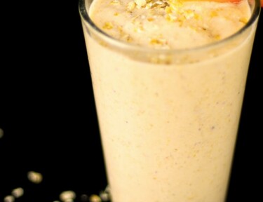 Peaches and Cream Oatmeal Smoothie in a tall glass with a peach slice on the rim.