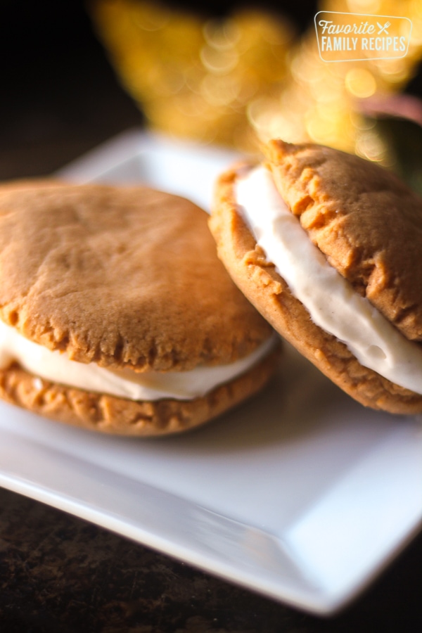 Pumpkin sandwich cookies stacked on top of each other on a white plate. 