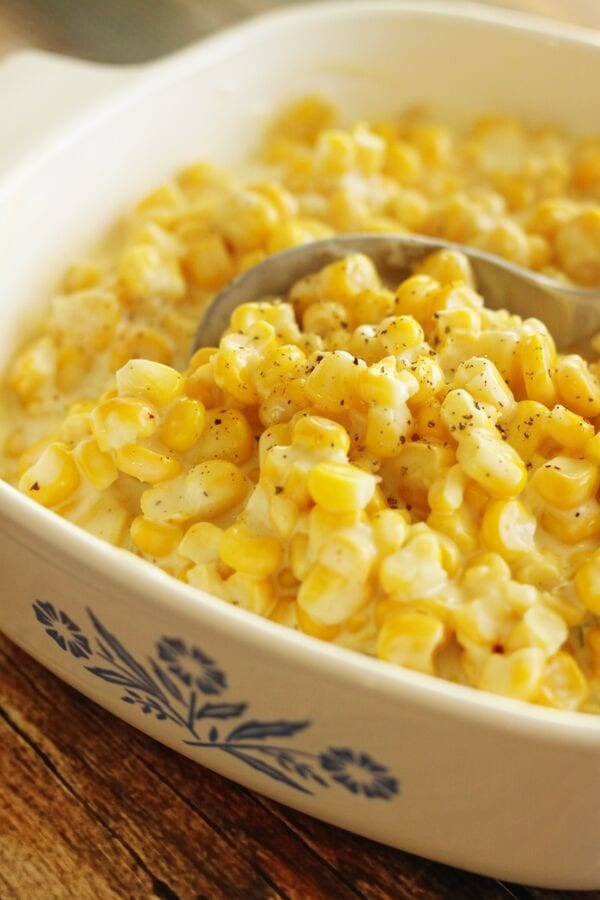 Slow Cooker Creamed Corn in a casserole dish with a serving spoon scooping out corn