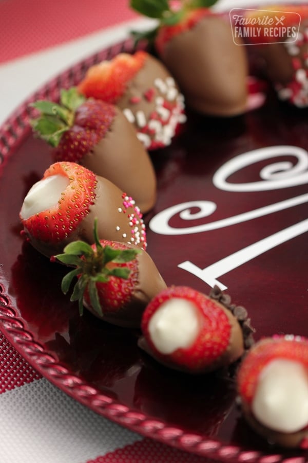 Cheesecake filled chocolate covered strawberries on a maroon plate.