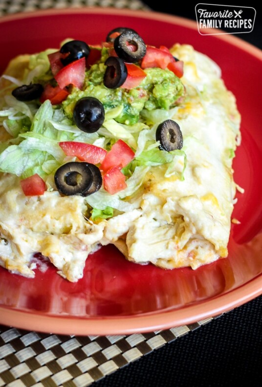 Chicken Enchiladas covered in lettuce, tomatoes, olives and guacamole on a red plate.