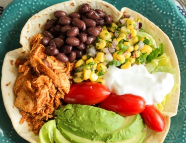 Chicken Taco Salad in a Tortilla Bowl with corn, beans, avocado, tomatoes, and sour cream in a blue bowl