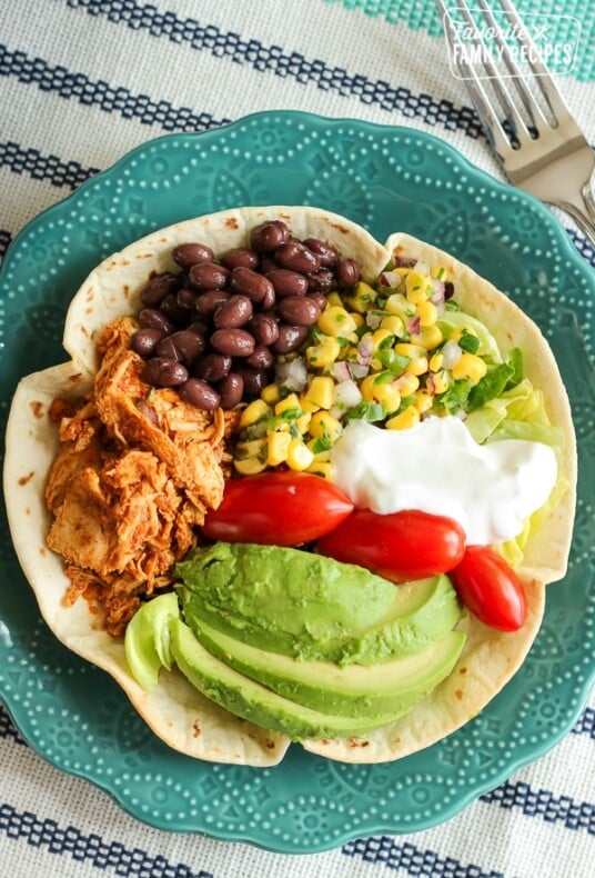 Chicken Taco Salad in a Tortilla Bowl with corn, beans, avocado, tomatoes, and sour cream in a blue bowl