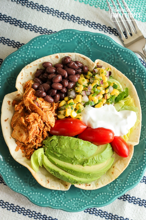 Chicken Taco Salad in a Tortilla Bowl with corn, beans, avocado, tomatoes, and sour cream in a blue bowl.