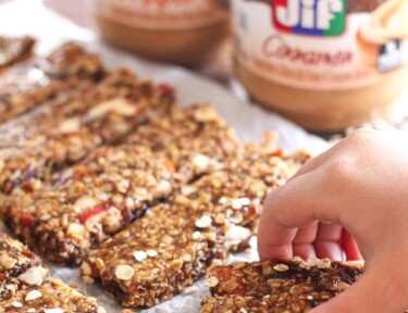 Breakfast idea of Cinnamon Peanut Butter Granola Bars lined up on parchment paper with peanut butter jars in the background.