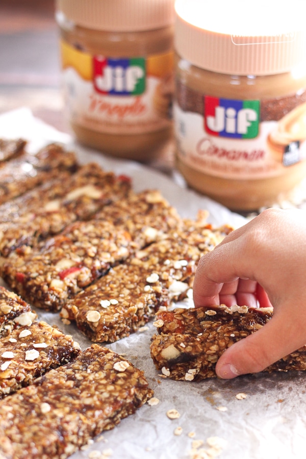 Cinnamon Peanut Butter Granola Bars lined up on parchment paper with peanut butter jars in the background.