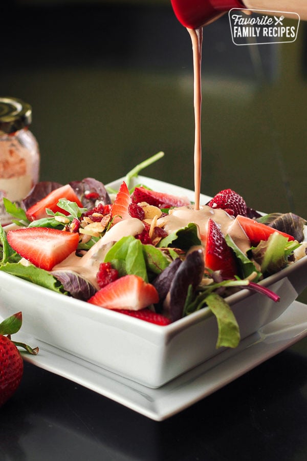 Creamy Strawberry Balsamic Dressing being poured onto a strawberry salad.