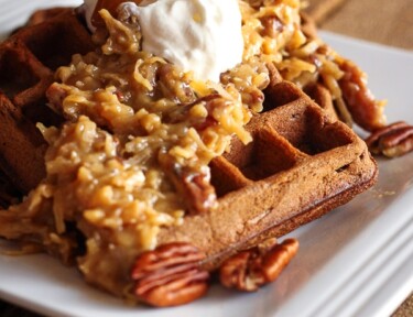 German Chocolate Waffles topped with Praline Pecan Syrup and whipped cream on a white plate.