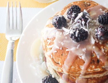 Blackberry Pancakes stacked on a white plate with a glass of milk on the side