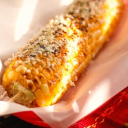Grilled Mexican Street Corn on a piece of paper in a red plate.