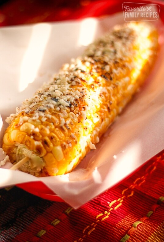 Grilled Mexican Street Corn on a piece of paper in a red plate.