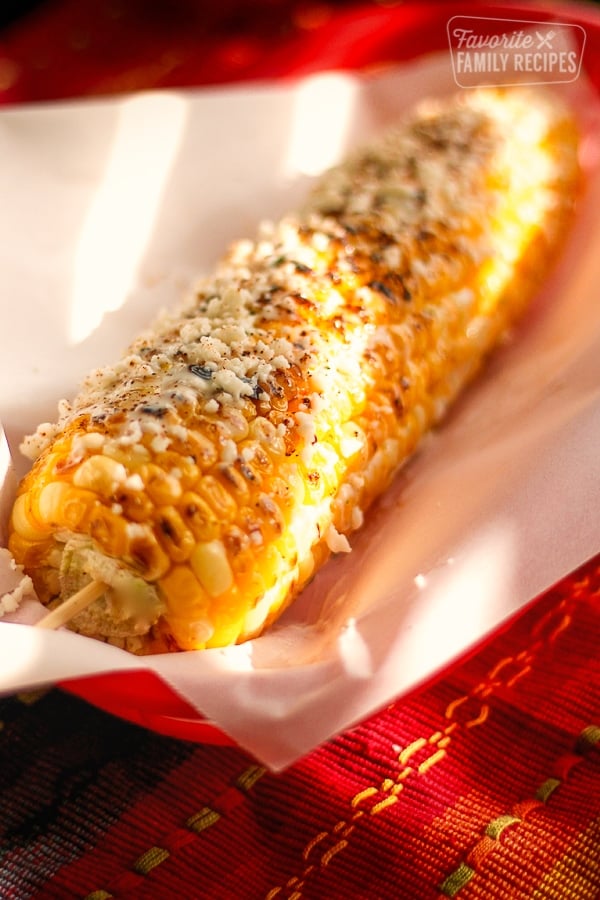 Grilled Mexican Street Corn on a piece of paper in a red plate.