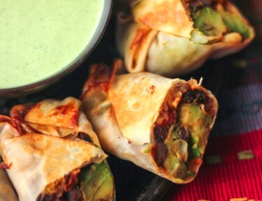 Healthy Baked Fiesta Avocado Egg Rolls on a plate with a dipping sauce on the side.
